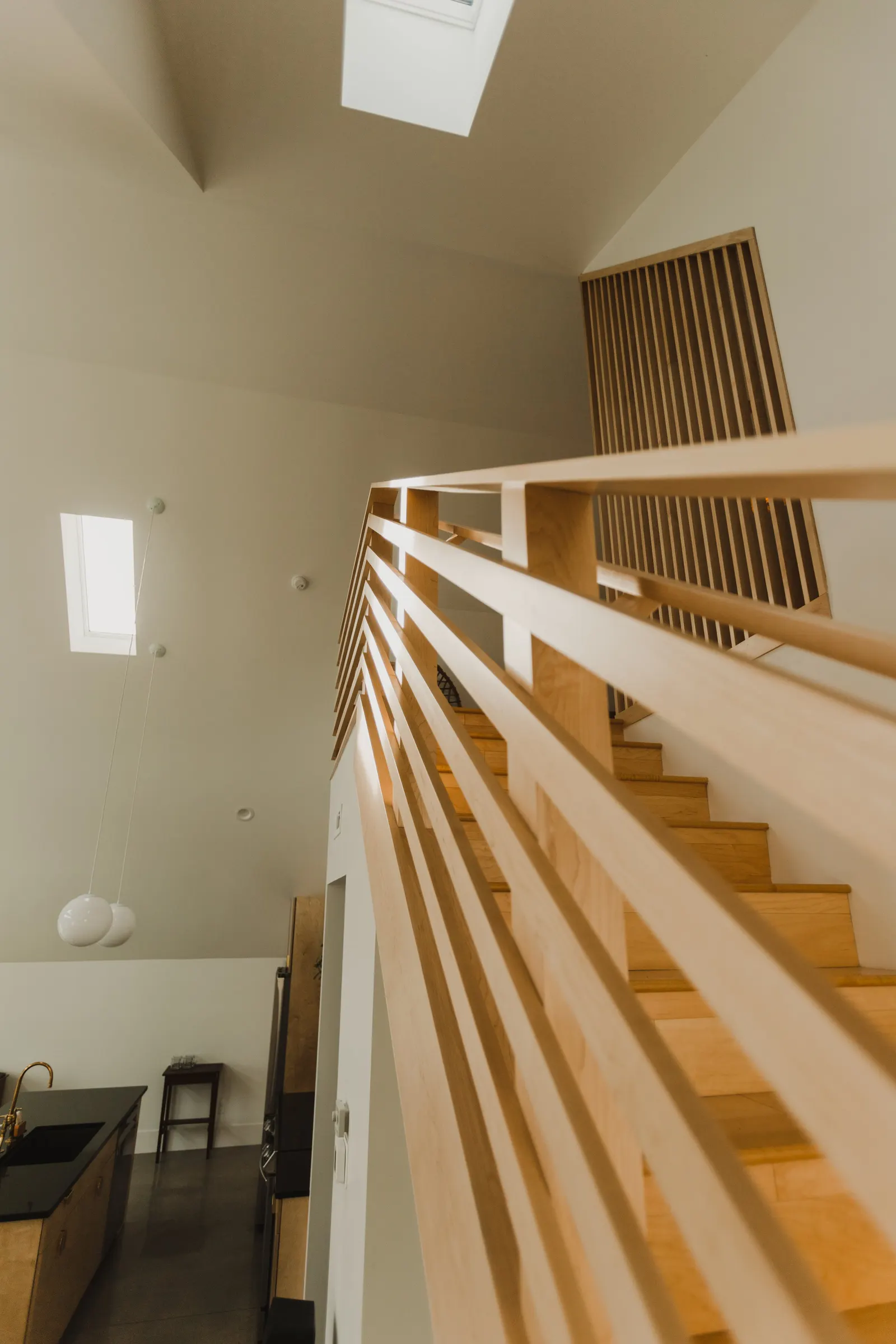 Interior view looking up at a wooden staircase with a railing, a ceiling skylight, and a hanging light fixture in a modern home.