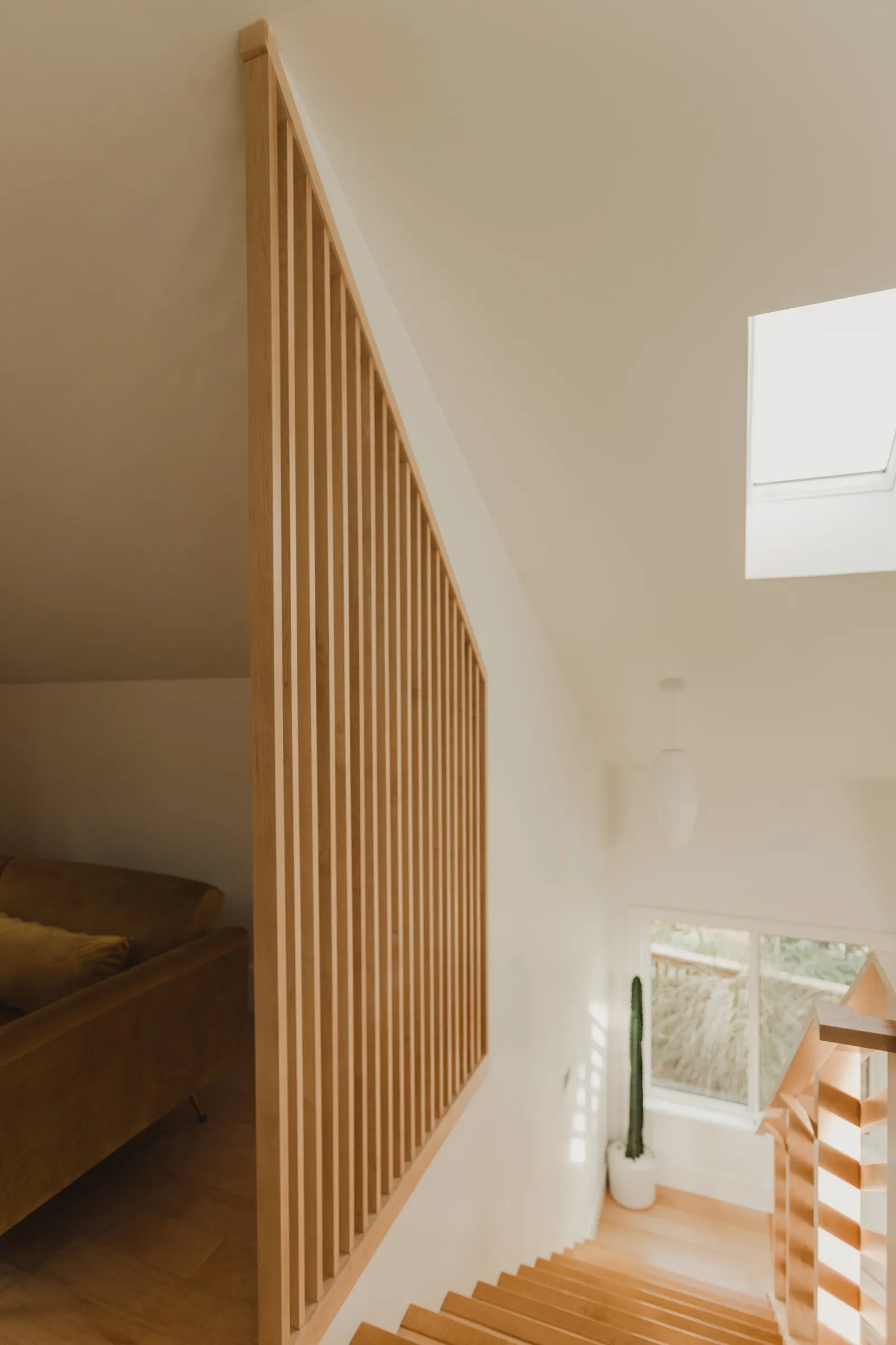 Interior view of a modern staircase with wooden steps, a tall cactus in a white pot, a large skylight, and a wooden railing.