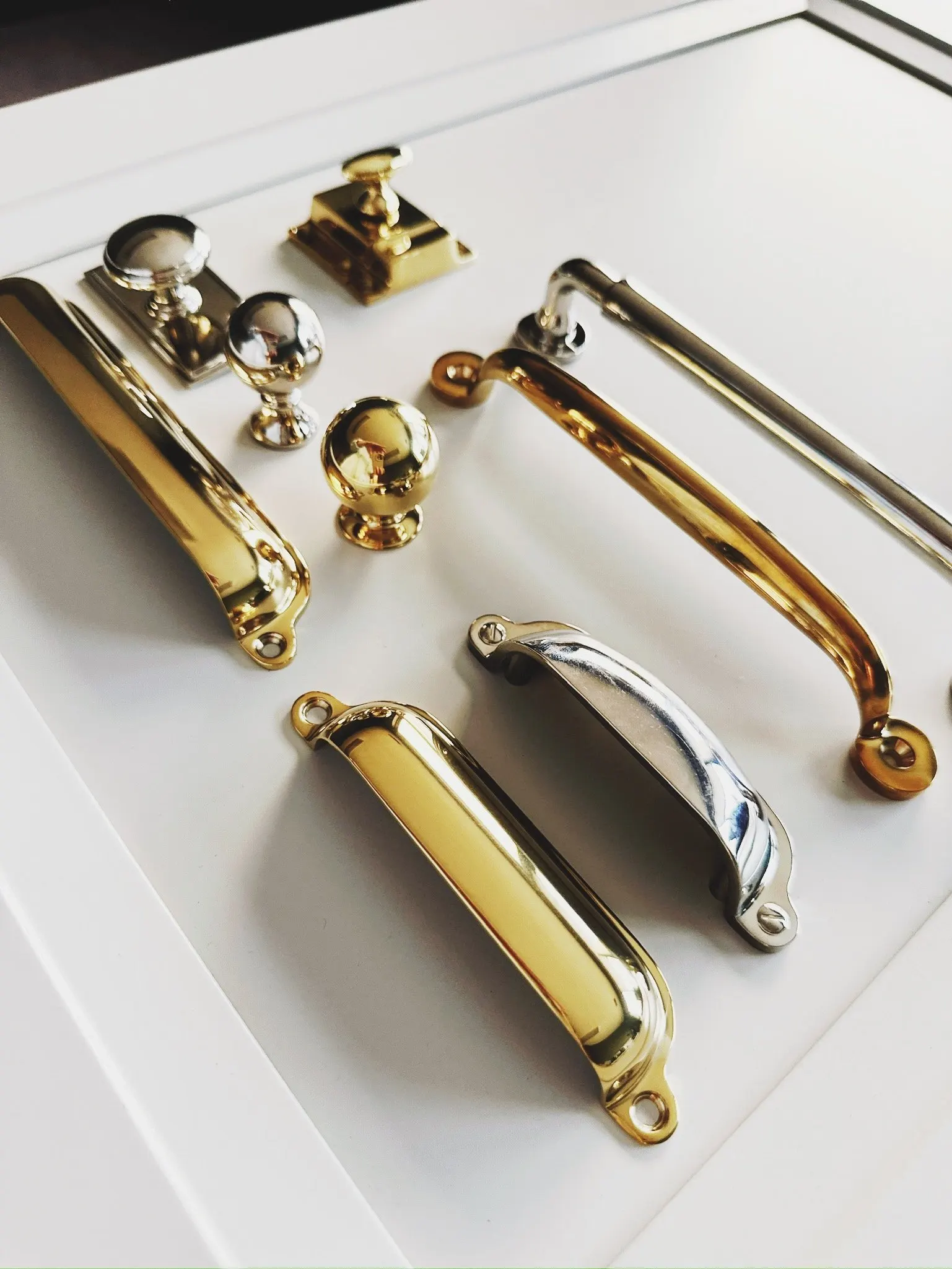 A collection of metal cabinet handles and knobs in gold and silver finishes on a white surface