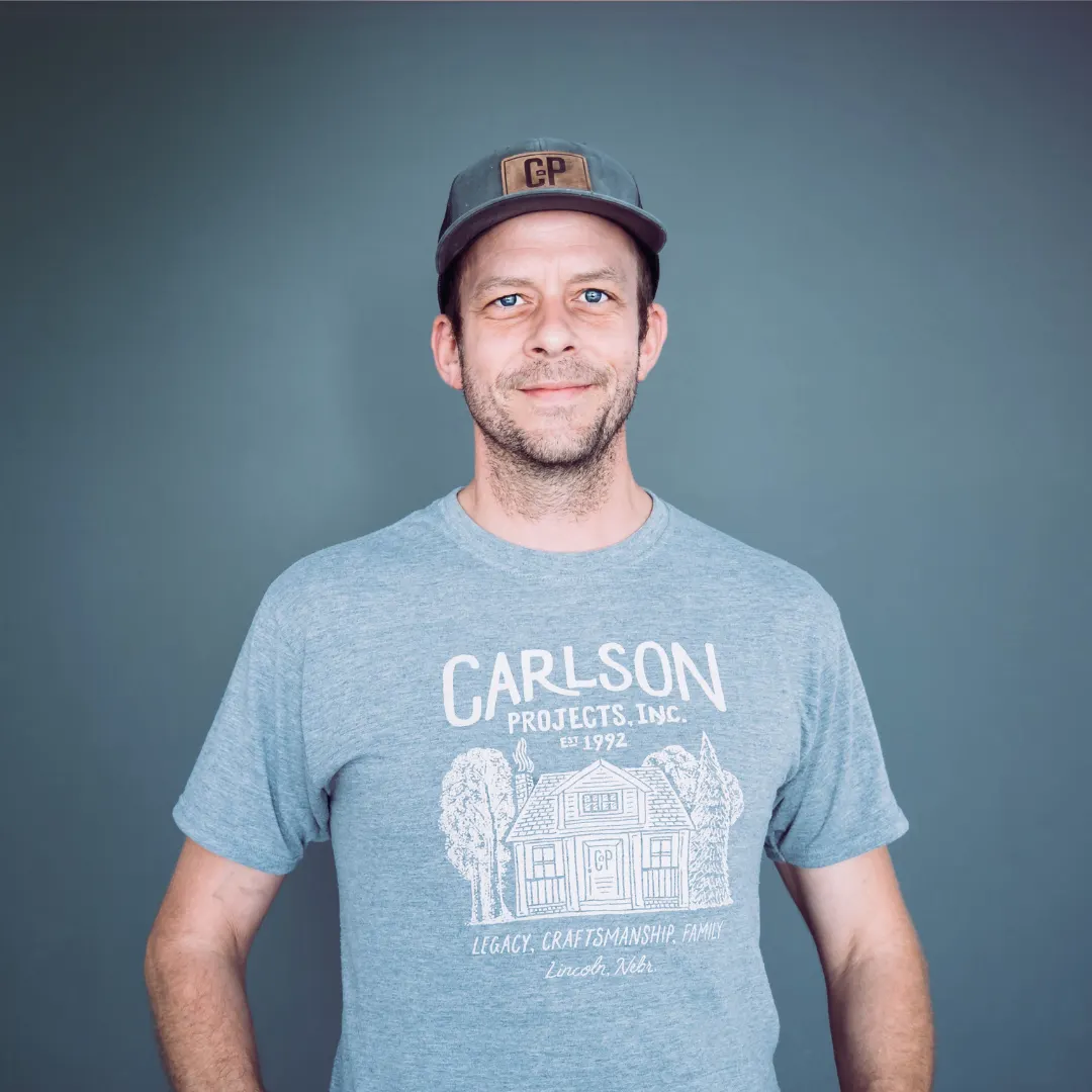 A man wearing a gray t-shirt with a house illustration and text, and a gray cap against a plain background. Project Manager, Rob.